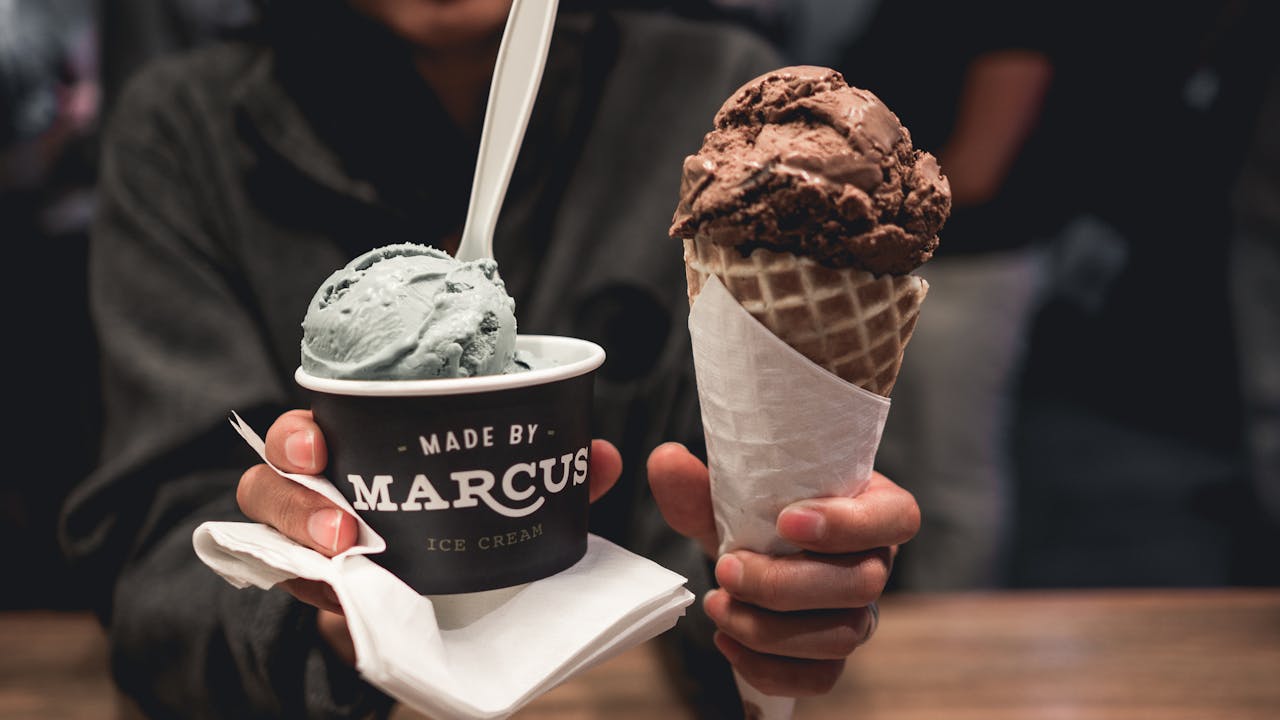 A close-up of chocolate cone and unique flavor ice cream cup held in hands.